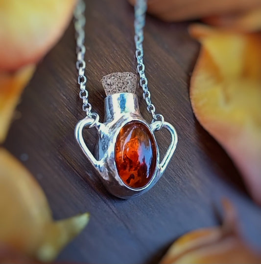 Potion bottle Necklace set with amber, on a wooden surface. Perfect for Spooky season, Halloween, Autumn, all the 'ber' months.