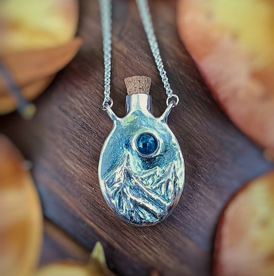Silver pendant bottle with blue gemstone on a wooden surface, fantasy inspired