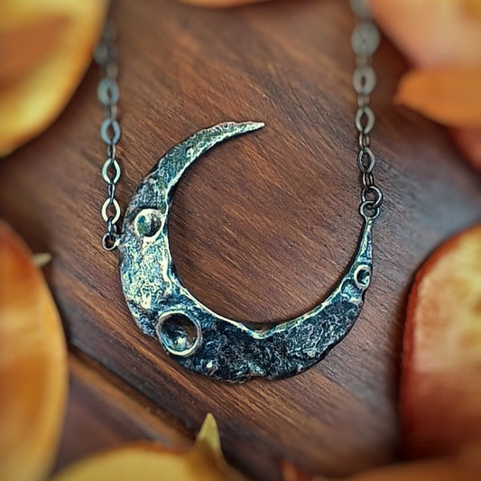 Silver crescent moon necklace on a wooden surface with dried autumn leaves.