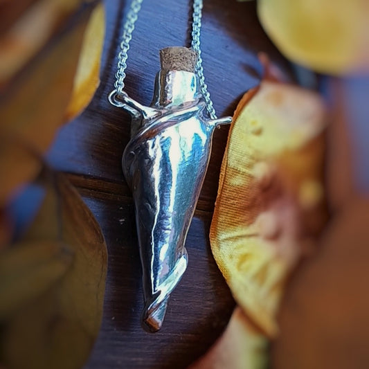 Silver potion bottle pendant on a chain against a wooden background