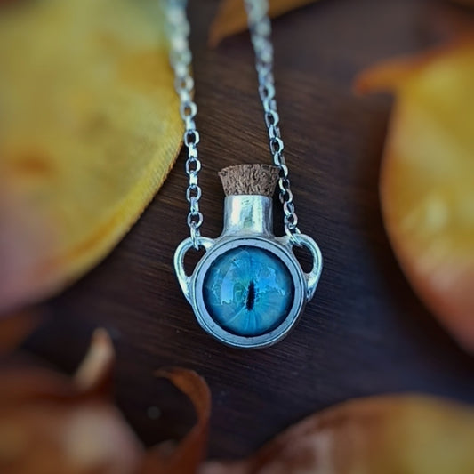 Silver necklace with a blue glass dragon eye potion bottle on a wooden surface