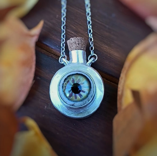 necklace with a yellowish-greenish glass eye potion bottle on a wooden surface