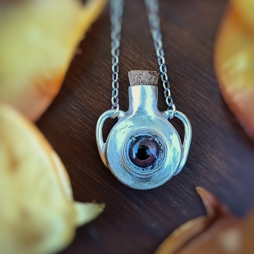 Silver potion bottle necklace with wine-colored glass eye and a cork stopper on a wooden surface
