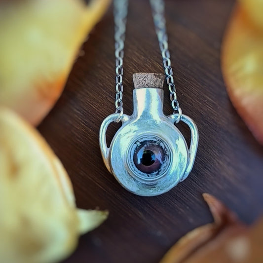 Silver potion bottle necklace with wine-colored glass eye and a cork stopper on a wooden surface