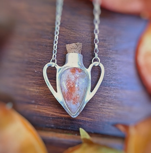 Heart-shaped potion pendant with sunstone and a cork stopper on a wooden surface