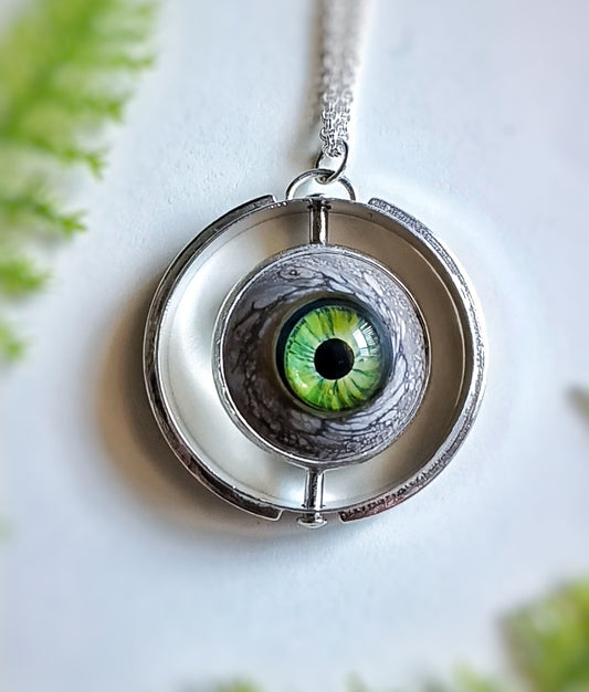 Kinetic jewelry, fidget spinner jewelry, this is a round sterling silver pendant set with a green glass eye that spins on a vertical axis.